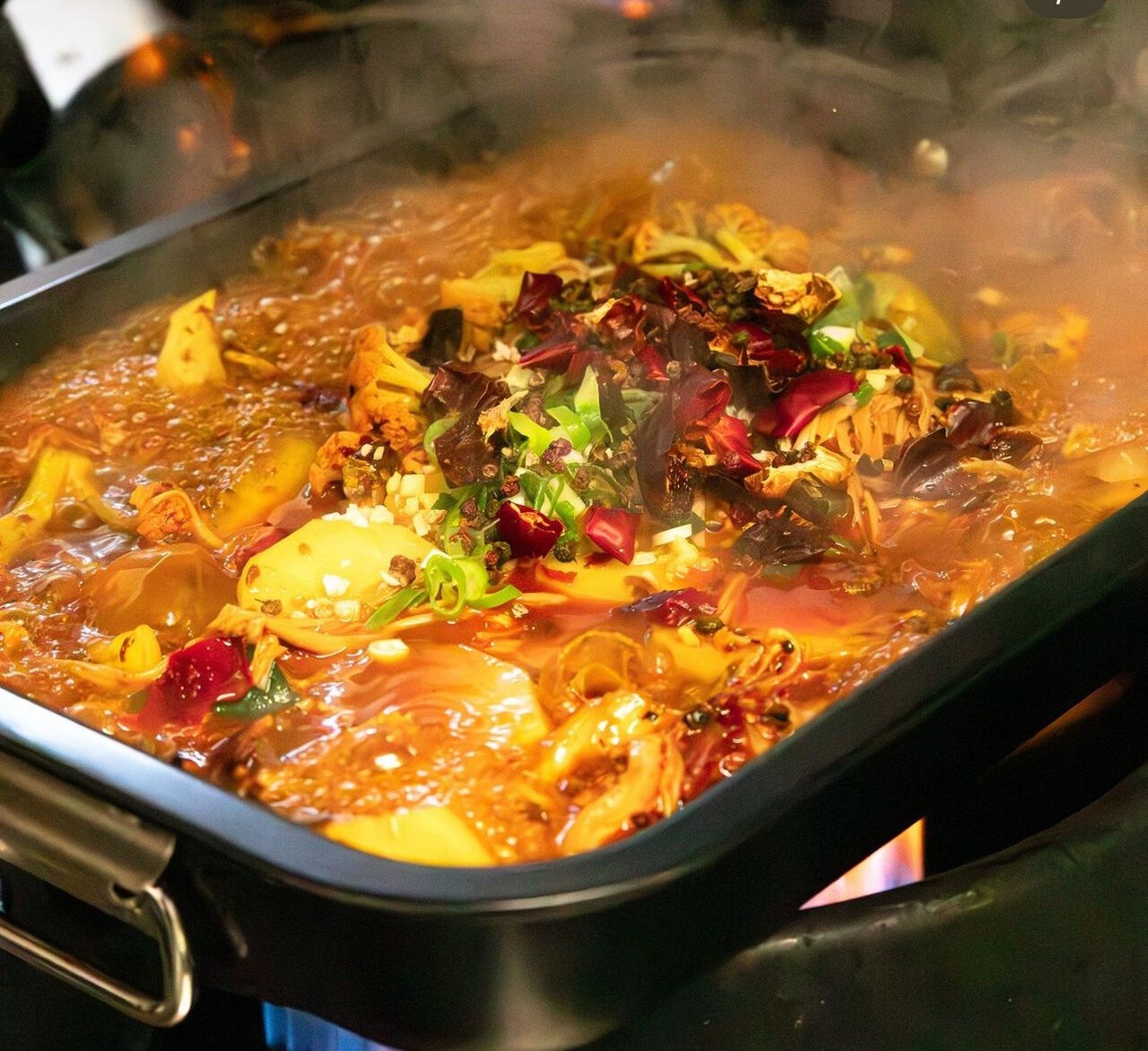 A steaming fire bowl on its burner, red broth with dried chillies.