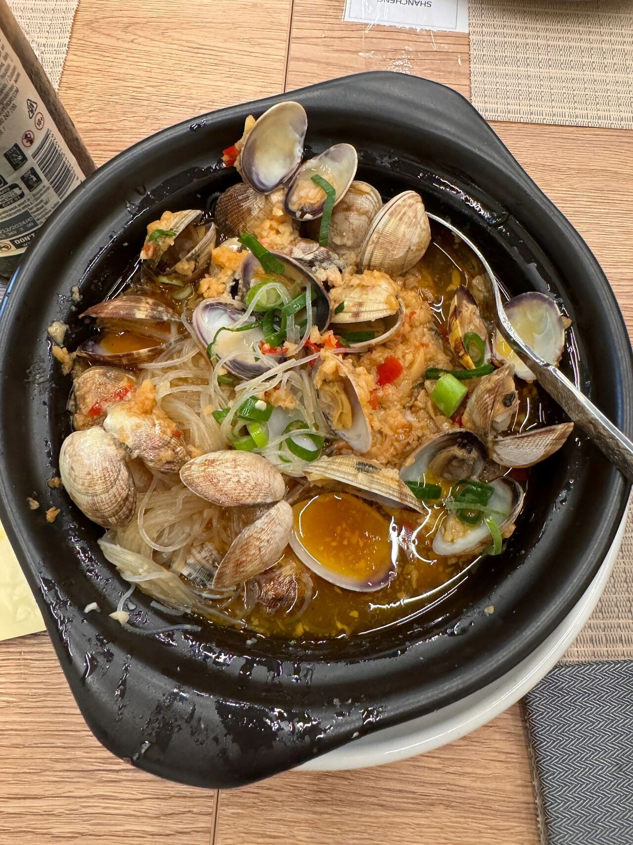 Clams with soy noodles in a black clay pot.