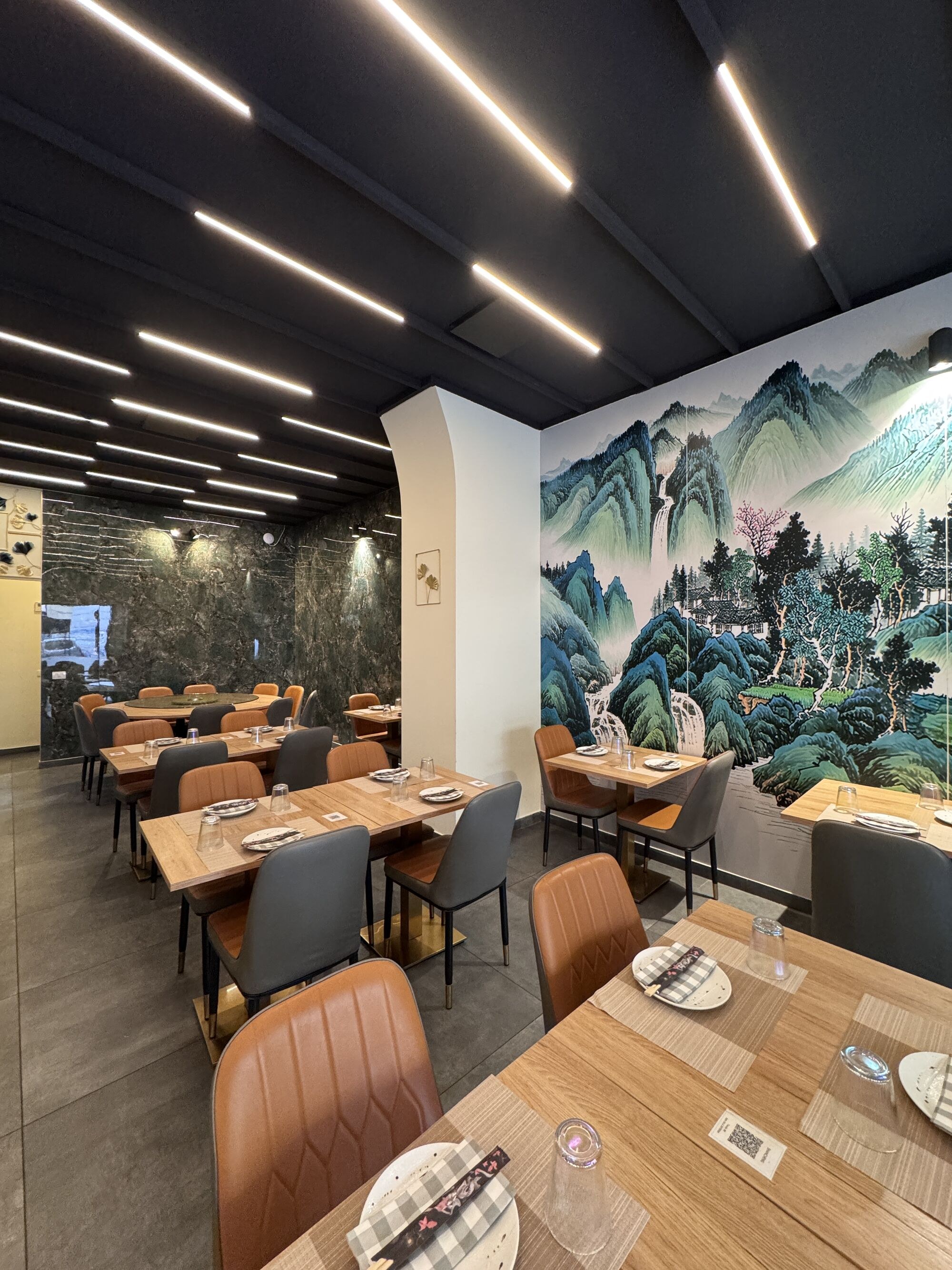 The dining room: one wall entirely painted with a jade-green Chinese mountain landscape, pale wood tables and tan leather chairs.